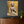 Laden Sie das Bild in den Galerie-Viewer, An der dunklen Wand hängt ein wunderschönes Bold von einem goldfarbenen Buddha. Das Bild wirkt sehr harmonisch und strahlt ein große Ruhe aus.