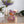 Laden Sie das Bild in den Galerie-Viewer, Spardose Bär Toto von Pomme Pidou in der Farbe grau blau mit buntem Muster sitz vor einem Blumenstrauß in der Farbe Flieder