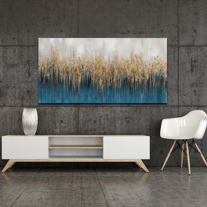 Ein abstarktes Kunstwerk hängt an einer tristen grauen Wand. Die Farben des Acryl-Gemäldes sind Gold und Blau