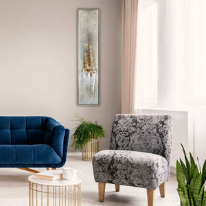 In einem Wohnzimmer hängt ein schmales Gemälde mit Rahmen an der Wand. das Gemälde ist in Erdtönen und der Farbe Gold handgemalt.