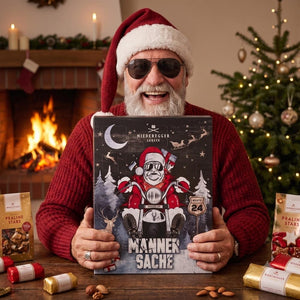 Ein Mann hält den Adventskalender Männersache von Niederegger Marzipan in den Händen. Der Mann trägt eine Nikolausmütze und eine Sonnenbrille genau wie auf dem Kalender.