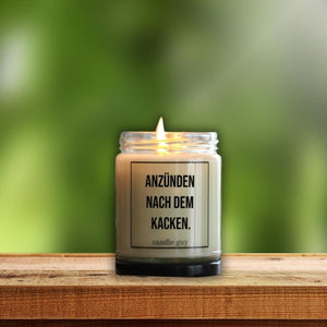 Anzünden nach dem Kacken steht auf einer brennenden Duftkerze im Glas.