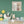 Liebevolle Babyzimmer Wandgestaltung mit dem Gemälde Das quadratische Alpaka-Wandbild hängt an einer salbeigrünen Wand über pastellfarbenem Kinderspielzeug, Dinosauriern und einem Hasen-Holzstuhl im skandinavischen Design.