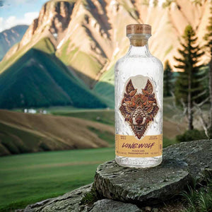 Auf einer schicken Flasche ist ein großer Wolfskopf. Darunter steht Lonewolf Peach & Passionfruit Gin. Im Hintergrund ist eine Alpenlandschaft.