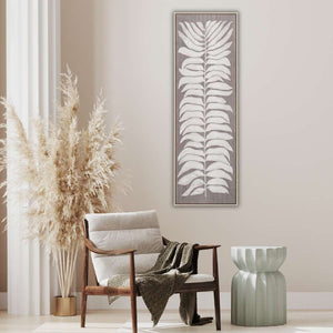 An einer beigen Wand im Wohnzimmer hängt ein gerahmtes Acrylbild mit hellen Blättern auf braunem Hintergrund.