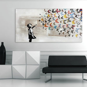 in großes, modernes Wandbild mit einem schwarzen Stencil-Mädchen-Silhouette, das bunte Schmetterlinge freilässt, auf strukturiertem Canvas, aufgehängt in einem modernen Wartezimmer einer Praxis mit weißem Sideboard und schwarzer Designer-Couch.