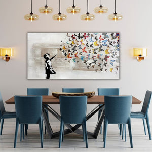 Großes Street-Art-Wandbild mit einer schwarzen Mädchen-Silhouette und bunten Schmetterlingen, aufgehängt in einem eleganten Esszimmer über einem Holztisch mit blauen Samtstühlen und modernen Glas-Pendelleuchten.