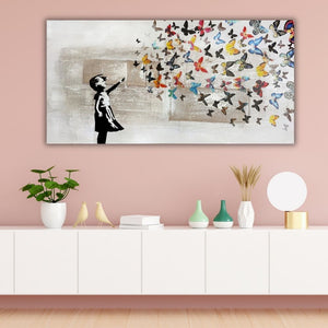 Großes Street-Art-Wandbild mit einem schwarzen Stencil-Mädchen und bunten Schmetterlingen, aufgehängt in einem modernen Wohnzimmer über einem weißen Sideboard mit Deko-Vasen auf altrosafarbener Wand.