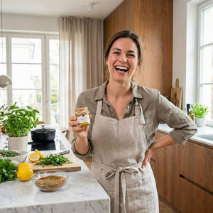Eine junge Frau in einer modernen Küche hält die Gewürzmischung Cafe de Paris von Gourmet Berner in der Hand und lacht