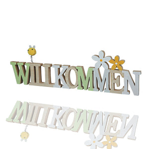 Schriftzug und Dekoelement Willkommen aus Holz. Die Farben des Schriftzugs sind Grün, braun, hellblau. Der Schriftzug hat auch noch Blumen