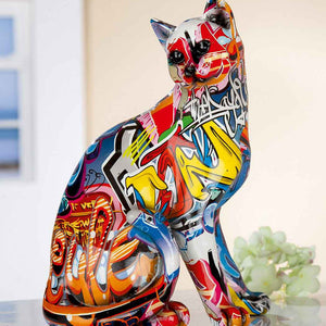 Die Dekofigur Katze ist sehr bunt und sitzt auf einem Sideboard