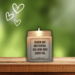 Auf einem Holzbrett im garten steht eine brennende Duftkerze mit dem Spruch: Scheiß auf Muttertag. ich liebe Dich jeden Tag.