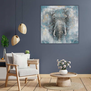 Ein mit Acrylfarbe gemalter Elefantenkopf schaut sanftmütig von einem quadratischen Gemälde welches an einer blauen Wand hängt.