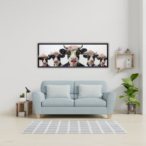 Modernes Panorama-Wandbild mit fünf lustigen Kühen, Sonnenbrillen und Perücken über einem hellblauen Sofa im Wohnzimmer – humorvolle Kunst für die Wanddeko.
