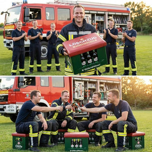 Feuerwehrleute mit Bierkastensitz Löschzug als Geschenk vor Einsatzwagen beim Anstoßen.