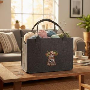 Auf dem Tisch steht ein grauer Filzshopper mit einer eingestickten Kuh mit Kopfschmuck. Im Filzshopper befindet sich Wolle. Die Filztasche ist ein idealer Aufbewahrungsort für Wolle.