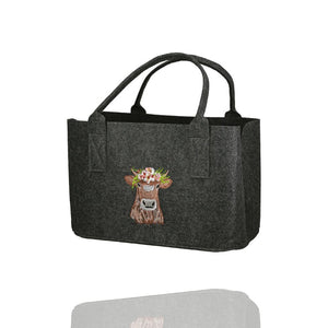 Auf einer dunkelgrauen Filztasche ist eine  braune Kuh mit buntem Kopfschmuck eingestickt. Der Filzshopper ist auf weißem Hintergrund