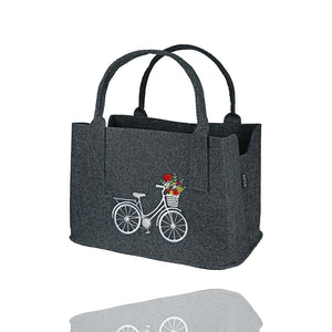 Auf einer Filztasche ist ein Fahrrad mit einem Korb voller bunter Blumen eingestickt.