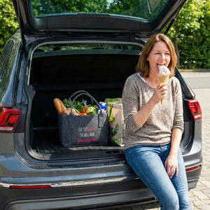 In einem Kofferraum eines SUV steht eine vollgepackte Filztasche auf der steht in der Farbe Pink. Die tut nix , die will nur shoppen. Neben ihr sitzt eine Frau die ein Eis isst.