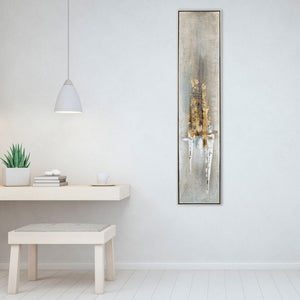 An einer weißen Wand hängt ein hhandgemaltes Gemälde in den Farben Gold, Weiß und in Erdtönen. Das schmale Gemälde hat einen zarten silberfarbenen Rahmen.