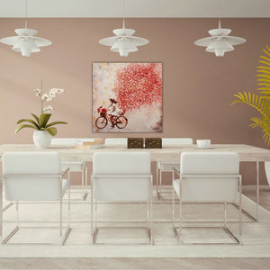 In einem modernen Esszimmer sieht man an der Wand in der Farbe Altrosa ein Gemälde vorwiegend mit der Farbe rot. das qudratische Bild zeigt eine junge Frau auf einem Fahrrad. Hinter dem Fahrad entsteht eine rote Wolke aus Blumen und Blütenblättern