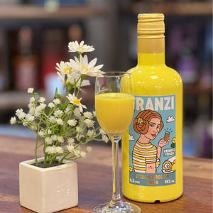 In einem schicken Glas ist der gelbe Franzbrötchenlikör mit Zitronenrollen Geschmack. Links daneben steht eine Frühlingsblume.