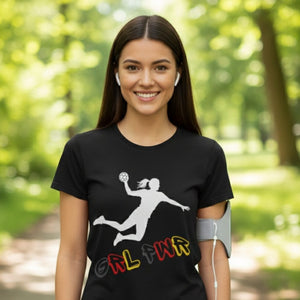 Deutscher Frauenhandball Fan T-Shirt in Schwarz, bedruckt mit der weißen Silhouette einer Handballspielerin beim dynamischen Sprungwurf. Darunter steht der Schriftzug "GRL PWR" in den Farben Schwarz, Rot und Gold. Eine lächelnde, junge Frau trägt das Shirt im Freien.