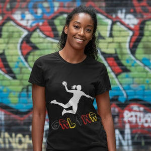 Deutscher Frauenhandball Fan T-Shirt in Schwarz mit dem weißen Motiv einer Handballspielerin im Sprungwurf. Darunter der Schriftzug "GRL PWR" in Schwarz, Rot und Gold (Deutschlandfarben). Eine lächelnde Frau trägt das Shirt vor einer farbenfrohen Graffiti-Wand im urbanen Umfeld.
