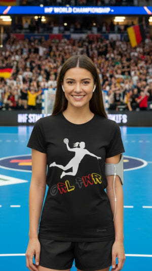 Eine junge Dame ist Handballfan und steht kurz vor dem Anpfiff mit ihrem Schwarz, Rot, Goldenem T-Shirt 
n der Handballarena. Auf dem Shirt ist eine Handballspielerin beim Torwurf zu sehen und es steht Girl Power auf dem Handball Fan T-Shirt.