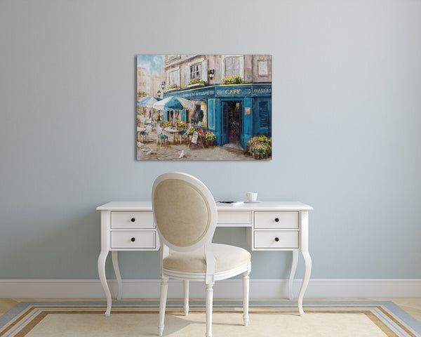 An der wand hängt ein Gemälde von einem blauen französischen Cafe. Ein Schreibtisch mit Stuhl steht vor dem Gemälde.