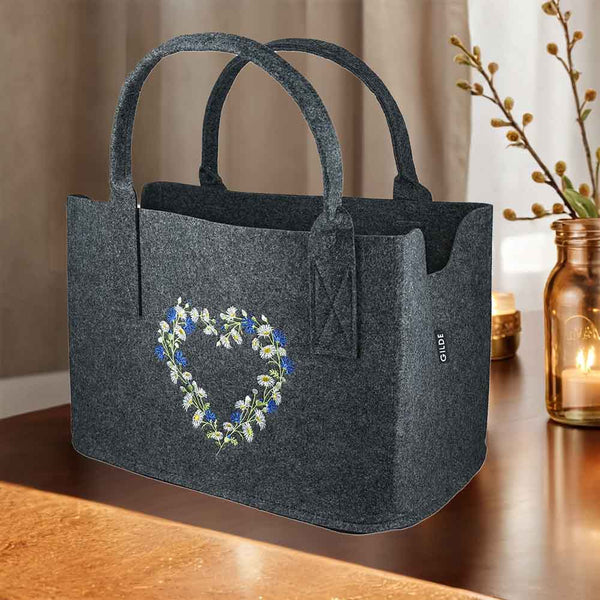 Bunte Wildblumen sind auf einer Filztasche in Herzform eingestickt. Die Tasche hat ein Etikett von Gilde.