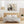 Das Acrylgemälde zeigt einen majestätischen Elefantenkopf in Nahaufnahme auf einem abstrakten Hintergrund in Beige-, Blau- und Goldtönen. Es hängt über einem Doppelbett mit hellem Holzrahmen in einem hellen, skandinavisch eingerichteten Schlafzimmer mit Holzmöbeln und Rattanlampenschirm.