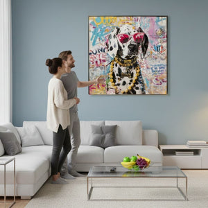 Junges Paar bewundert ein farbenfrohes Pop-Art-Gemälde eines Dalmatiners an einer hellblauen Wand in einem modern eingerichteten Wohnzimmer mit weißen Möbeln, weißen Gardinen, einer Stehleuchte und einem Glastisch mit Obstkorb.