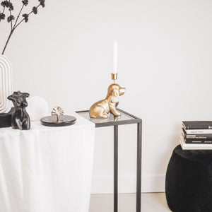 Ein goldfarbener Kerzenständer in Form eines Dackels sitzt auf einem Beistelltisch mit Glasplatte.
