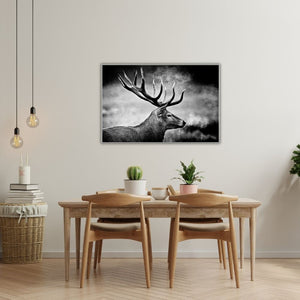 In einem Esszimmer aus Naturhölzern hängt an der wand ein stolzer Hirsch. er schreitet durch den Nebel. das Bild ist in einem Rahmen und in schwarz weiß.