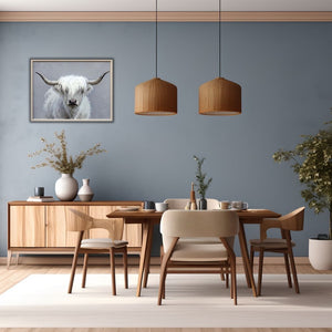 Ein Esszimmer mit hellem Holz. An der blauen Wand hängt ein Bild mit Rahmen. Auf dem Bild sieht man den Kopf eines schottischen Hochlandrinds in der Farbe Weiß. Die Frisur des Cattles besteht aus Kunsthaar.