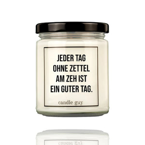 Eine Duftkerze in einem Glas mit schwarzem Deckel. Auf dem Glas steht: Jeder Tag ohne Zettel am Zeh ist ein guter Tag. Die Kerze ist von Candle Guy