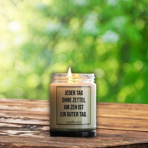 Auf einem Gartentisch steht ein Windlicht welches auch eine Duftkerze ist. Auf ihr steht: Jeder Tag ohne Zettel am Zeh ist ein guter Tag