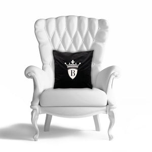 Auf einem weißen Ledersessel ist das edle schwarze Kissen vom BRIDEMAKER. Auf dem Kissen ist sein Logo mit der Krone eingestickt.