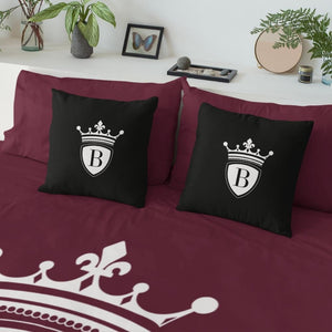 Auf einem Bett mit roter Bettdecke stehen zwei schwarze Kissen mit dem BRIDEMAKER Logo