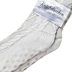 Kuschelsocken mit Teddy und ABS Sohle steht auf dem Schild, welches an den Stricksocken mit Zopfmuster hängt.