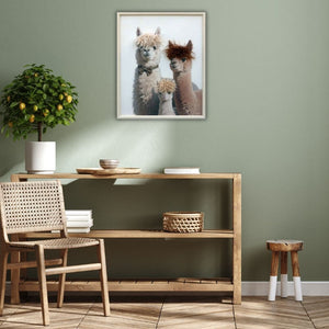 An einer grünen Wand hängt ein Bild mit Rahmen. Auf dem Bild sind drei lamas mit Kunstfell Perücken zu sehen. 