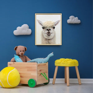 Ein Kinderzimmer mit einer blauen Wand. An der Wand hängen weiße Wolken und ein Bild von einem Lama mit einer Figur aus Kunstfell.