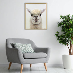 Ein grauer bequemer Sessel steht in einem Wohnzimmer vor einer weißen Wand. Über dem Sessel hängt ein Bild von einem Lama mit Kunstfell.