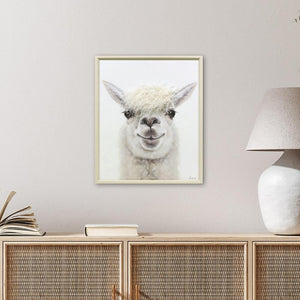 Über einem Sideboard aus Rattan hängt ein helles Bild im Hochformat. Ein flauschiges Lama mit einer lustigen Frisur und großen Knopfaugen schaut mich an.