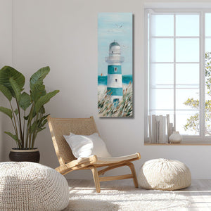 Helles, modernes Zimmer mit einem schmalen vertikalen Acrylgemälde eines blau-weißen Leuchtturms an der Wand. Neben dem Bild befinden sich eine große Pflanze, ein geflochtener Holzsessel und zwei weiße Poufs in einer lichtdurchfluteten Atmosphäre.