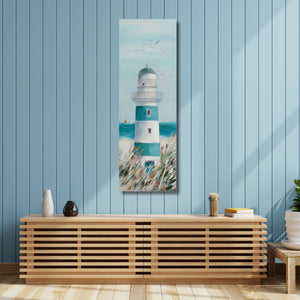 Ein schmales Acrylgemälde eines blau-weißen Leuchtturms hängt an einer blau getäfelten Wand über einem Sideboard aus hellem Holz. Das Gemälde zeigt den Leuchtturm inmitten von hohen Gräsern vor einem hellblauen Himmel mit fliegenden Möwen. Auf dem Sideboard stehen dezente Dekorationsgegenstände wie zwei kleine Vasen, ein Stifthalter und einige Bücher, während seitlicher Lichteinfall eine gemütliche Atmosphäre im Raum schafft.