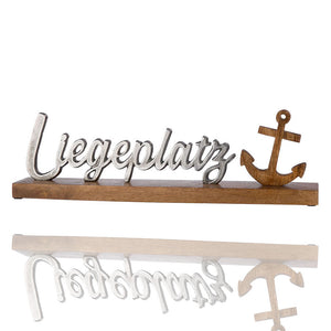 Schriftzug Liegeplatz aus Aluminium der an einem Stück Holz befestigt ist. Wunderschönes Dekoelement für Deun zu Hause. Ein Holzanker ziert dieses Wohraumaccessoire.