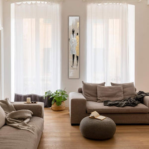 In einem Wohnzimmer zwischen zwei Fenstern an einer schmalen Wand hängt ein Acrylgemälde in Gold und Silber von zwei Models auf einer Modenschau.