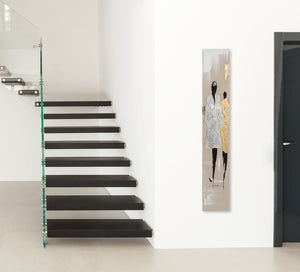 An einer Wand im Flur hängt hochkant ein schmales Leinwandbild in Silber und Gold. Es zeigt eine Modenschau mit zwei Models.